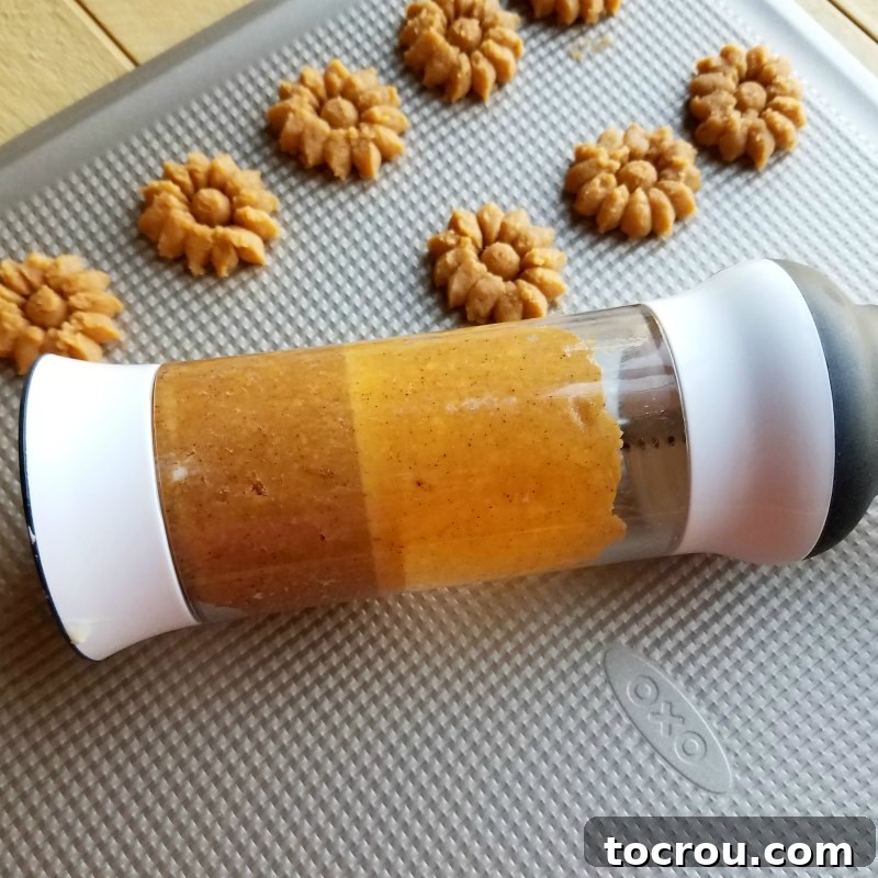 Using a cookie press makes these chili cheese crackers fun and easy to shape. cookie press filled with cracker dough and some crackers pressed out onto cookie sheet.
