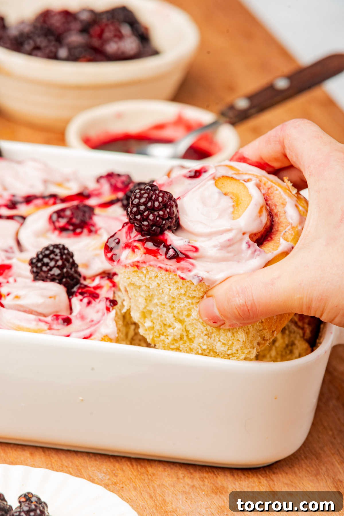 Hand grabbing big blackberry sweet roll out of the pan.