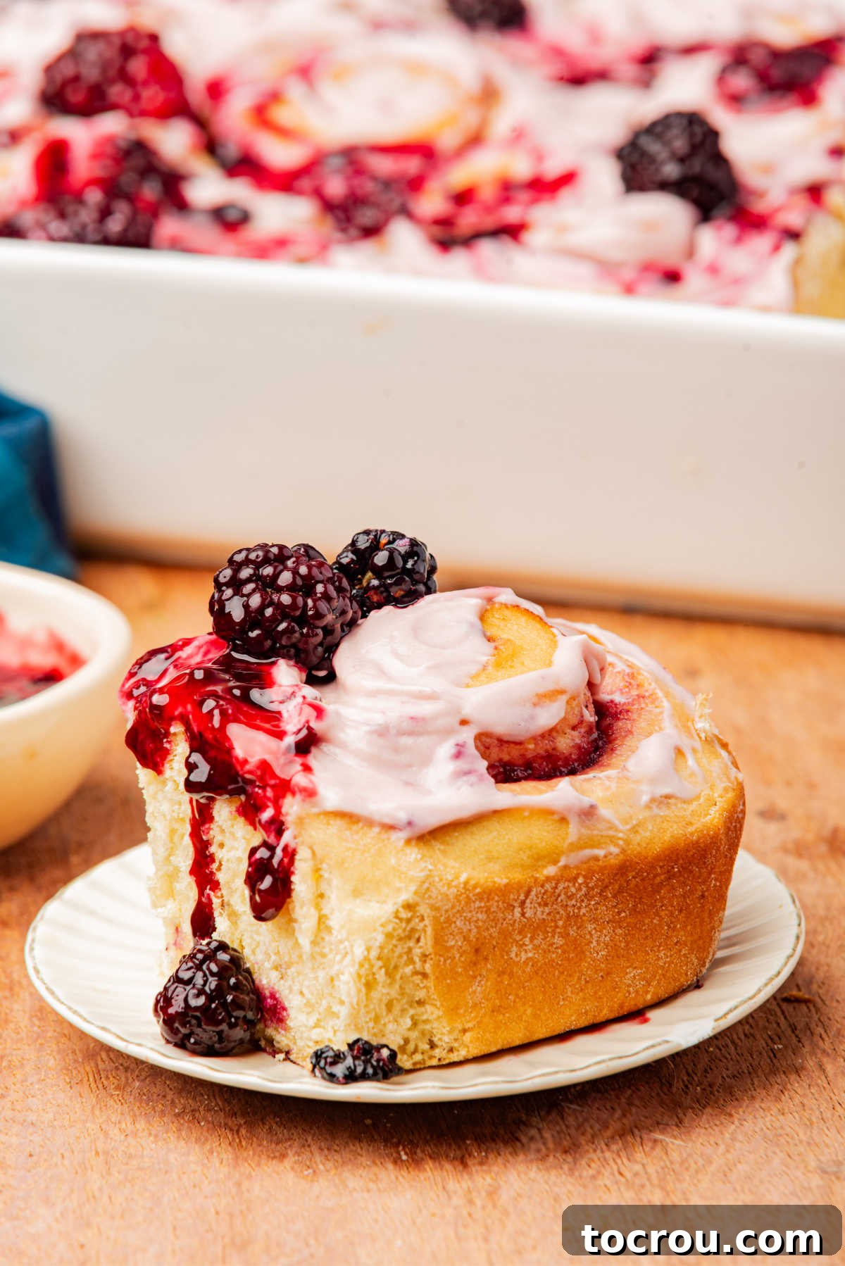 Fluffy blackberry sweet roll with cinnamon roll swirl filled with blackberry compote and topped with blackberry cream cheese frosting and a few more blackberries.