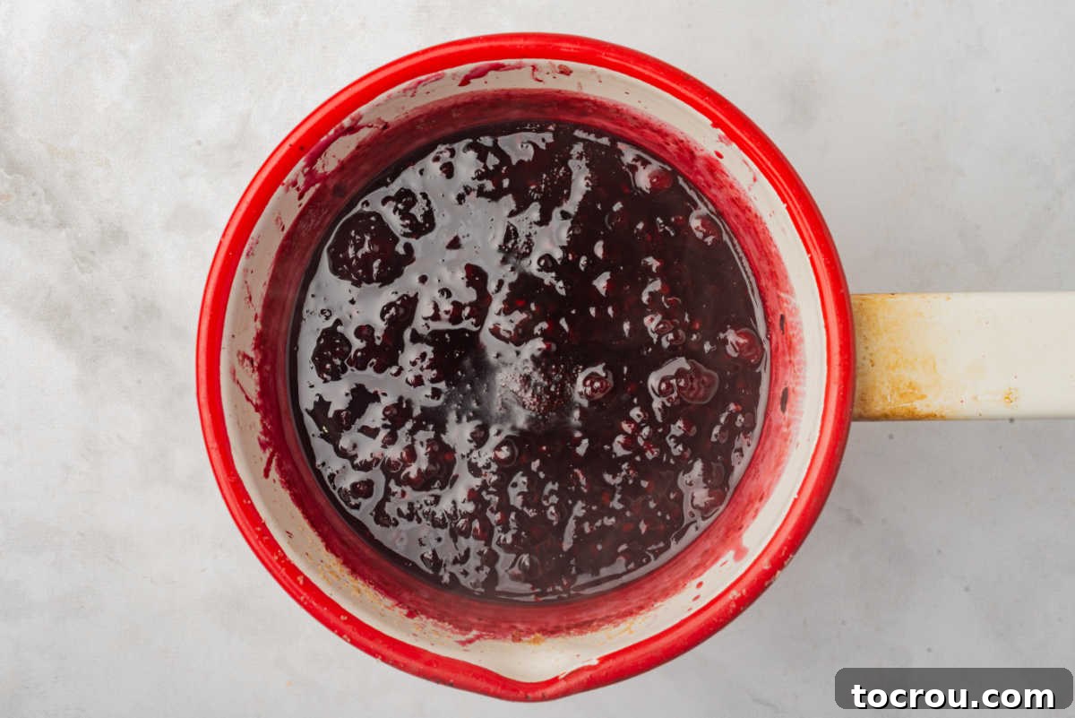A saucepan filled with simmering blackberry compote, visibly thickening on the stove as the berries release their juices.