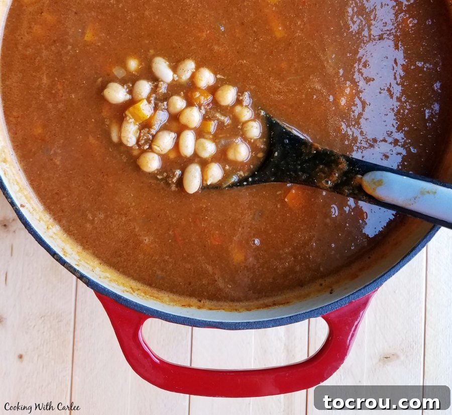 A spoonful of rich Apple Ale Pumpkin Chili, showcasing ground turkey and beans, ready to be served from a large enameled cast iron pot. spoon full of beans and ground turkey over big enameled cast iron pot of apple ale pumpkin chili.