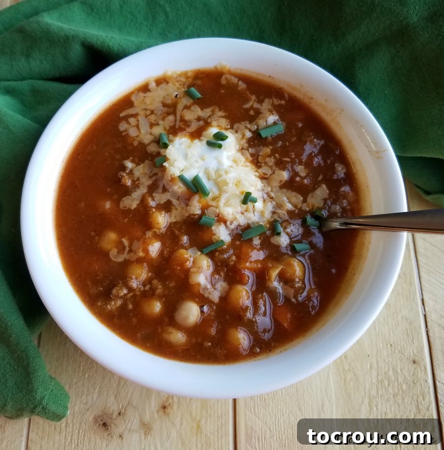 A delectable bowl of Apple Ale Pumpkin Chili, richly topped with shredded cheese, a dollop of sour cream, and fresh chives, ready to be savored. bowl of apple ale pumpkin chili topped with shredded cheese, sour cream and chives on top.