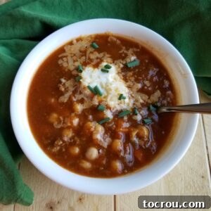 Apple Ale Pumpkin Chili, richly topped for serving. bowl of apple ale pumpkin chili topped with shredded cheese, sour cream and chives on top.