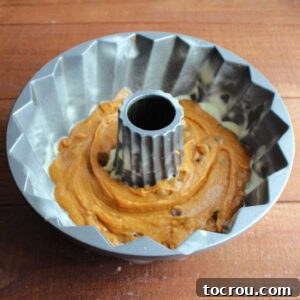 Harvest Pumpkin Bundt Cake with Cream Cheese Core 13 Half of the pumpkin cake batter spread evenly into the bottom of a meticulously greased Bundt cake pan, ready for the next layer.