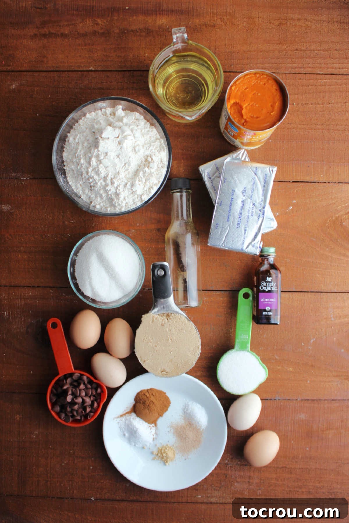 Harvest Pumpkin Bundt Cake with Cream Cheese Core 4 A vibrant display of fresh ingredients, including flour, sugars, pumpkin puree, oil, eggs, softened cream cheese, chocolate chips, and a medley of spices like cinnamon, ginger, and nutmeg, prepared for baking a delicious Bundt cake.
