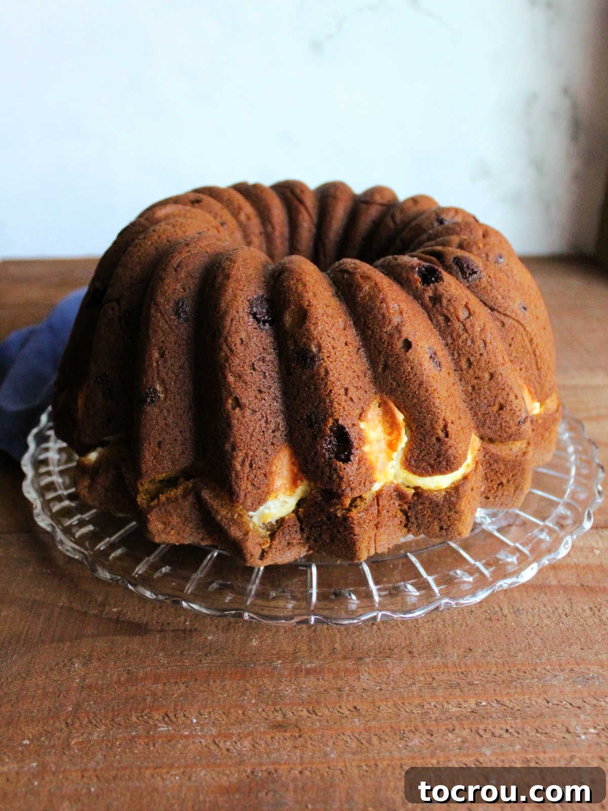 Harvest Pumpkin Bundt Cake with Cream Cheese Core 5 A beautifully baked cream cheese-filled pumpkin Bundt cake resting elegantly on a glass serving platter, highlighting its golden crust and classic shape.
