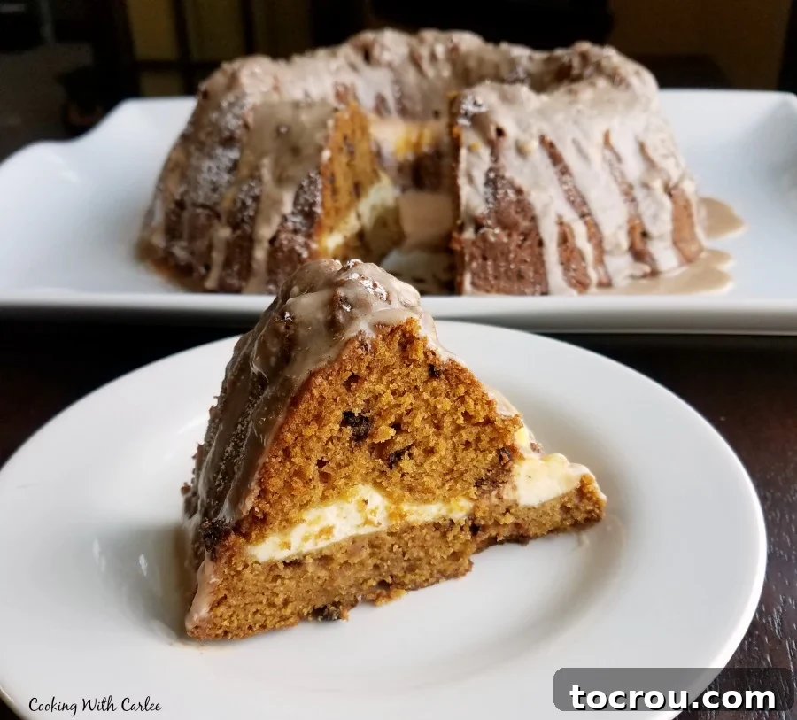 Harvest Pumpkin Bundt Cake with Cream Cheese Core 7 A close-up of a generous slice of pumpkin chocolate chip Bundt cake, showcasing a distinct ribbon of creamy white cream cheese filling running through its center.