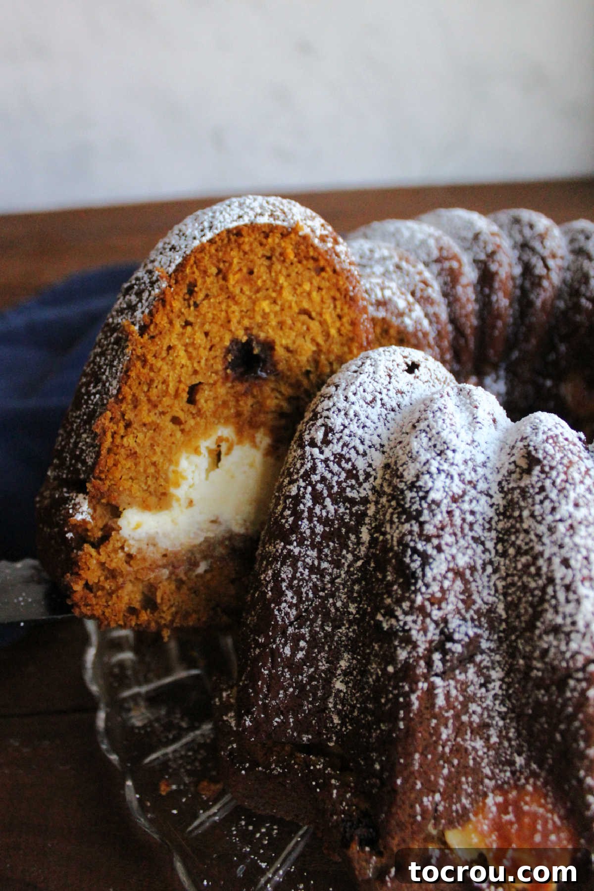 Harvest Pumpkin Bundt Cake with Cream Cheese Core 8 A hand gently lifting a slice of cream cheese-filled pumpkin Bundt cake from the main cake, showcasing its perfect serving readiness.