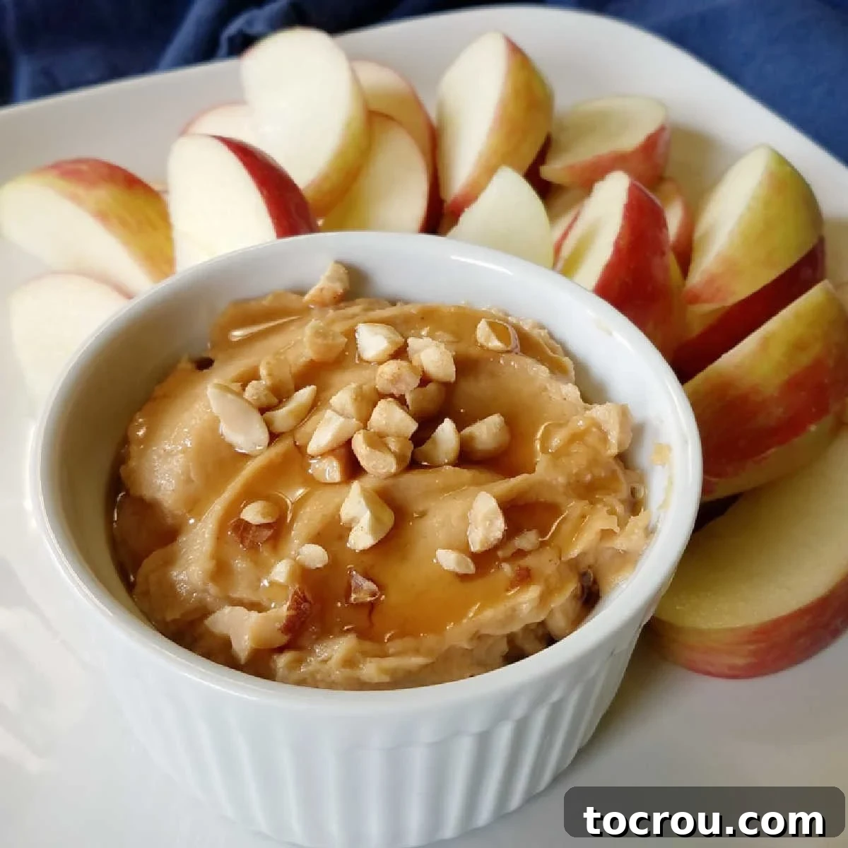 Delicious Peanut Butter Yogurt Fruit Dip with Apple Slices Ramekin of peanut butter yogurt dip topped with a drizzle of honey and chopped peanuts served on a plate with apple slices.