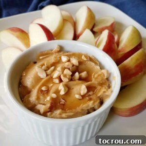 Peanut Butter Yogurt Fruit Delight 2 Ramekin of peanut butter yogurt dip topped with a drizzle of honey and chopped peanuts served on a plate with apple slices.