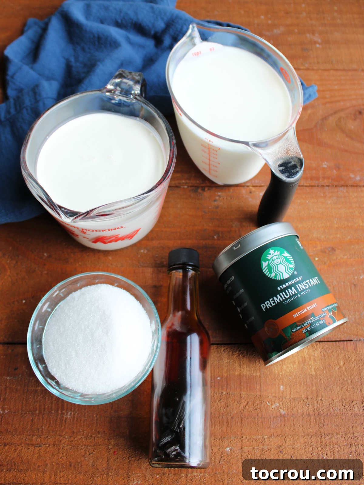 A collection of essential ingredients including fresh milk, granulated sugar, aromatic instant coffee, pure vanilla extract, and rich heavy cream, all neatly arranged and ready to be transformed into delicious homemade ice cream.