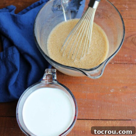 Mixing bowl with sugar, coffee, and milk mixture being whisked, positioned next to a measuring cup containing heavy cream, ready for the next step.