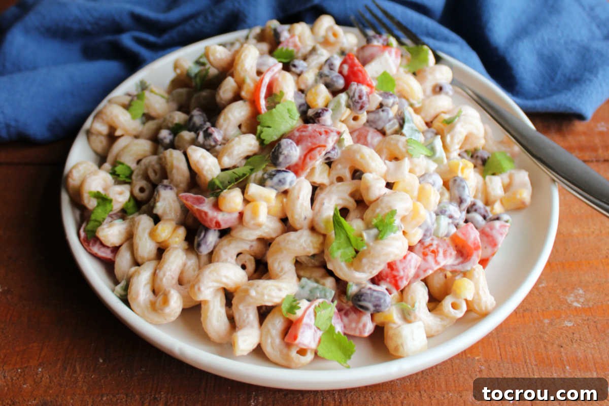 Close-up shot of creamy Cowboy Pasta Salad with corkscrew pasta, black beans, corn, peppers, and tomatoes, glistening with BBQ dressing.