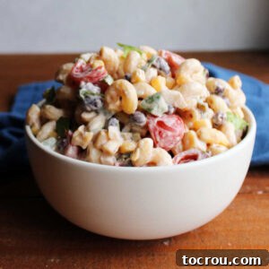 Bowl piled high with cowboy pasta salad with swirled pasta in creamy bbq dressing with tomatoes, peppers, corn, black beans and more mixed in.