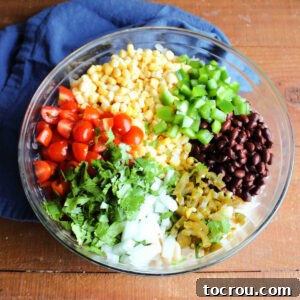Pieces of grape tomatoes, corn, bell pepper, green beans, pickled jalapeno peppers, onion, and cilantro ready to be stirred into pasta salad.