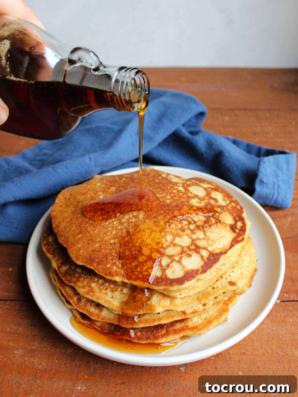 Pouring maple syrup on a stack of whole wheat sourdough pancakes. 
