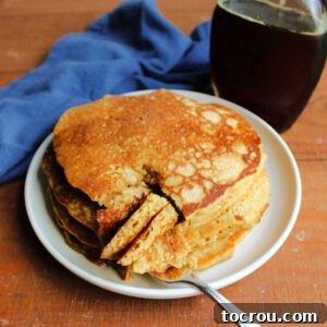 Stack of sourdough pancakes with a wedge cut out and pancakes on fork showing fluffy interior with a bottle of maple syrup in the background.