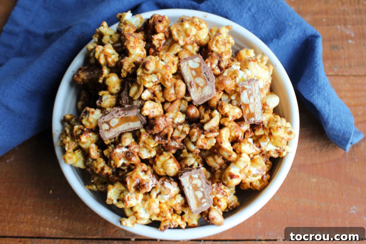 Big bowl piled with homemade snickers popcorn with caramel, peanuts and bits of candy bar. 