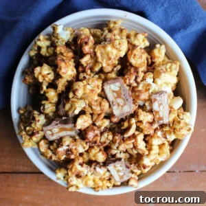 Bowl of snickers popcorn with crunchy caramel corn, peanuts, and bits of snickers bars throughout.