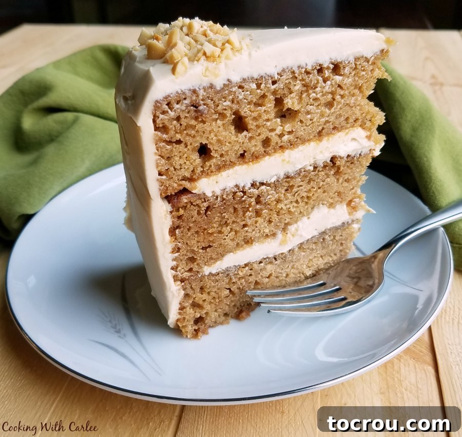 A generous slice of applesauce cake with visible layers of cake and soft caramel cream cheese frosting, served on a dessert plate with a fork, ready to be enjoyed.