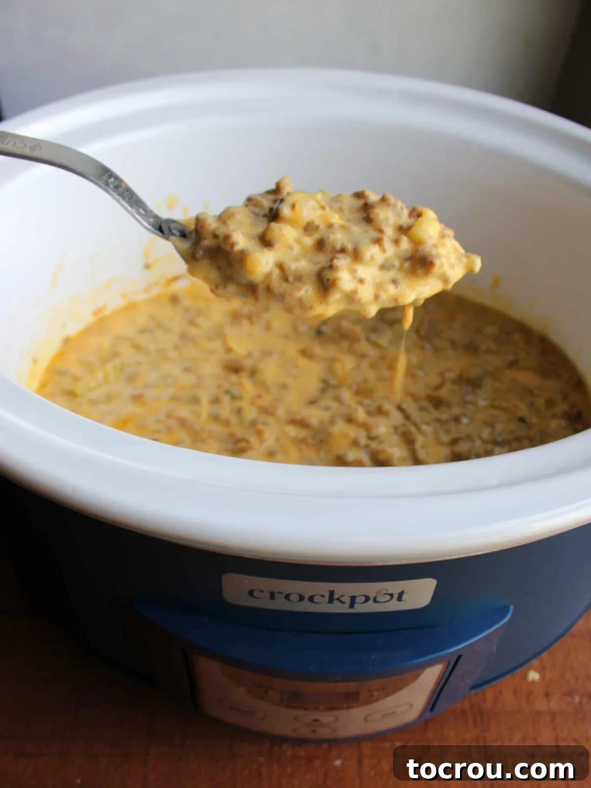 Serving spoon lifting a generous scoop of the creamy, melted crockpot cheeseburger mixture from the slow cooker.