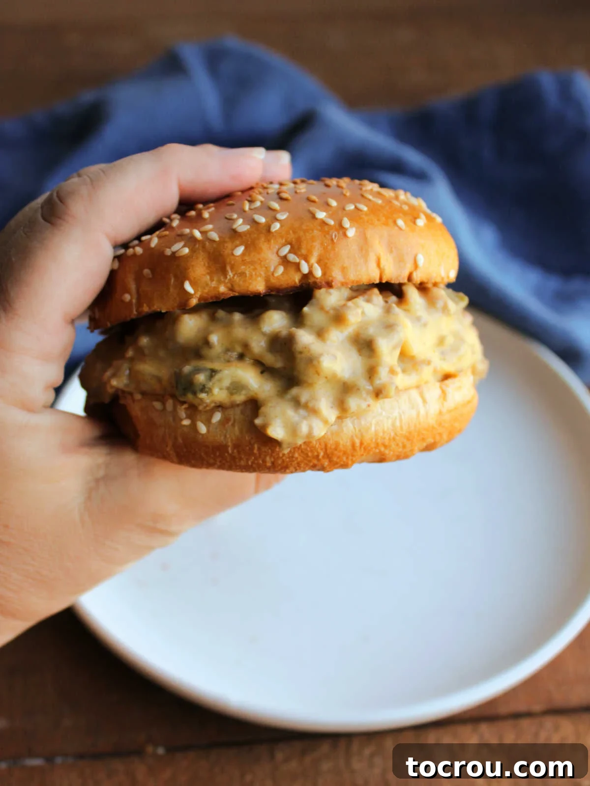 Hand holding a crockpot cheeseburger sloppy joe, ready for a delicious bite.