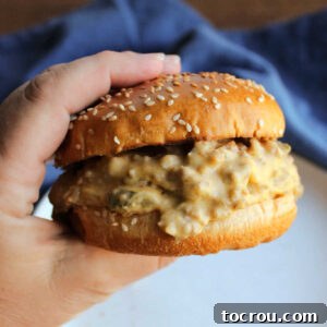 Hand holding a toasted sesame bun filled with crockpot cheeseburger mixture, ready to eat.