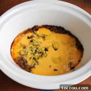 Cooked mixture in crockpot showing melted cheese on top of ground beef, before stirring.