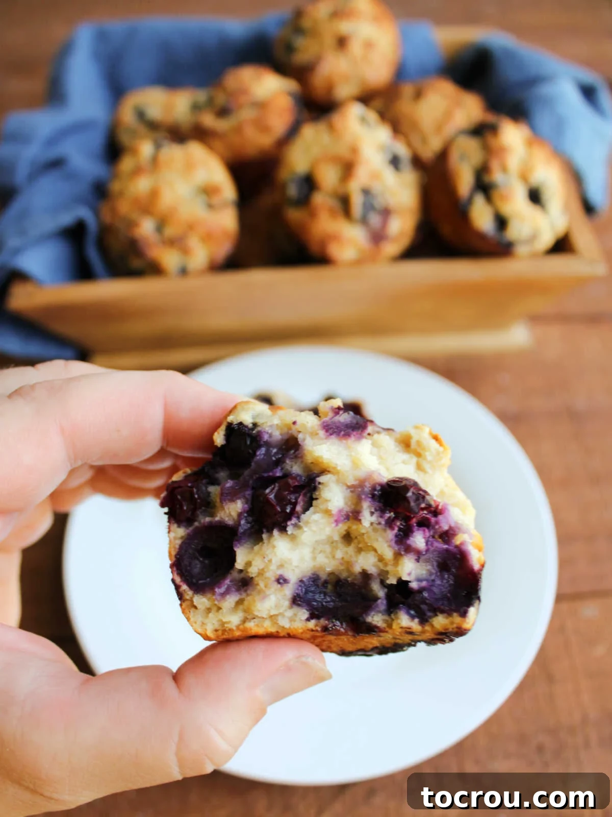 Hand holding half of a blueberry sourdough muffin showing soft texture and lots of blueberries inside. 