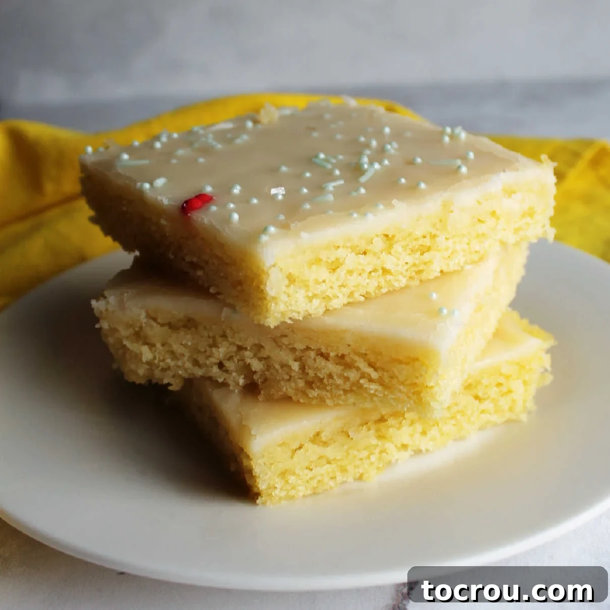 This Lemon Texas Sheet Cake is perfect for feeding a crowd. It is so easy to make and has just the right amount of lemon flavor. Take it to your next BBQ, family reunion or potluck! Stack of slices of lemon Texas sheet cake with smooth icing and sprinkles on top.