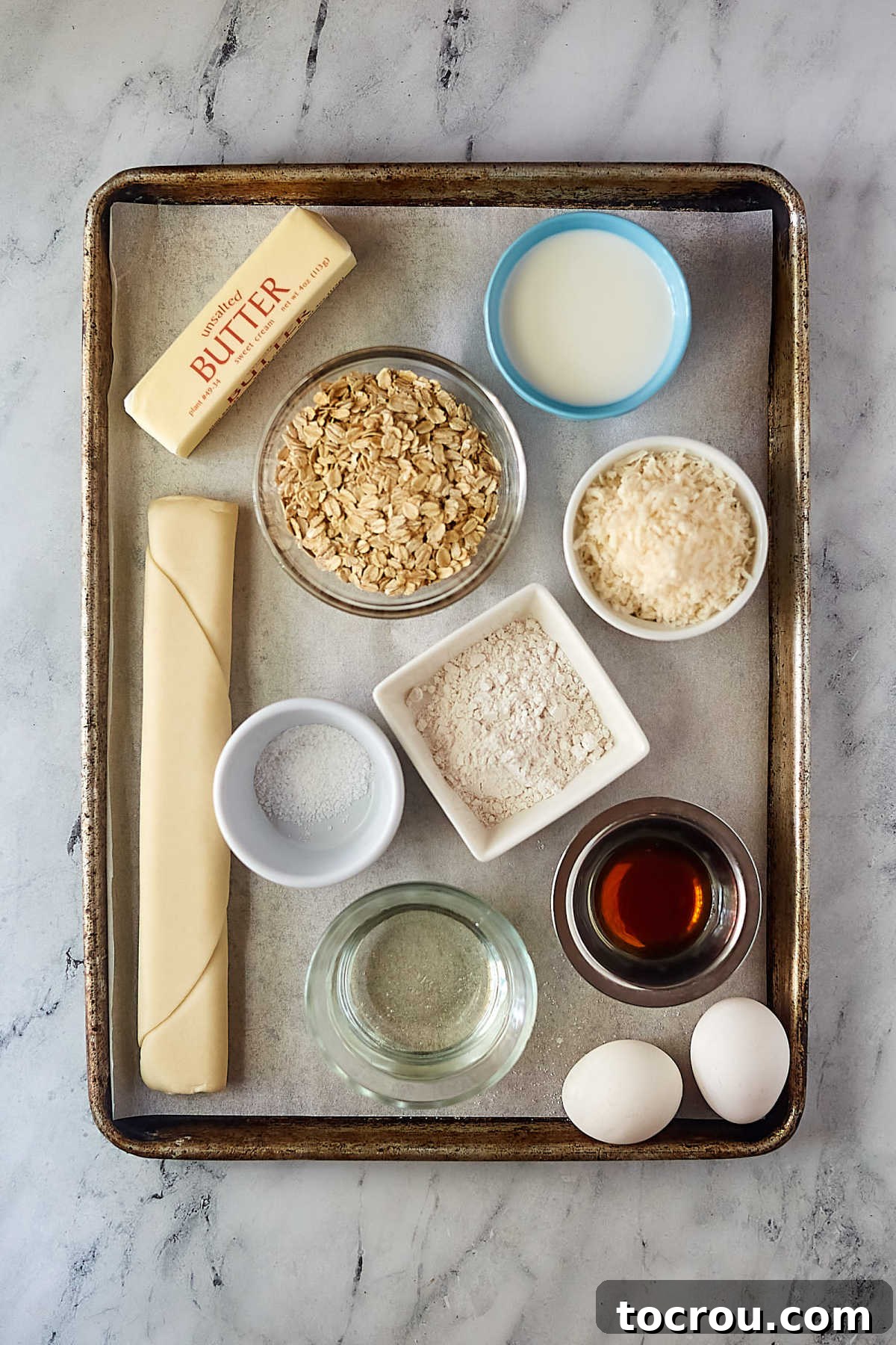 A collection of fresh ingredients laid out, including a pie crust, shredded coconut, rolled oats, eggs, butter, vanilla extract, light corn syrup, milk, and all-purpose flour, neatly arranged for making a delicious old-fashioned oatmeal pie with coconut.