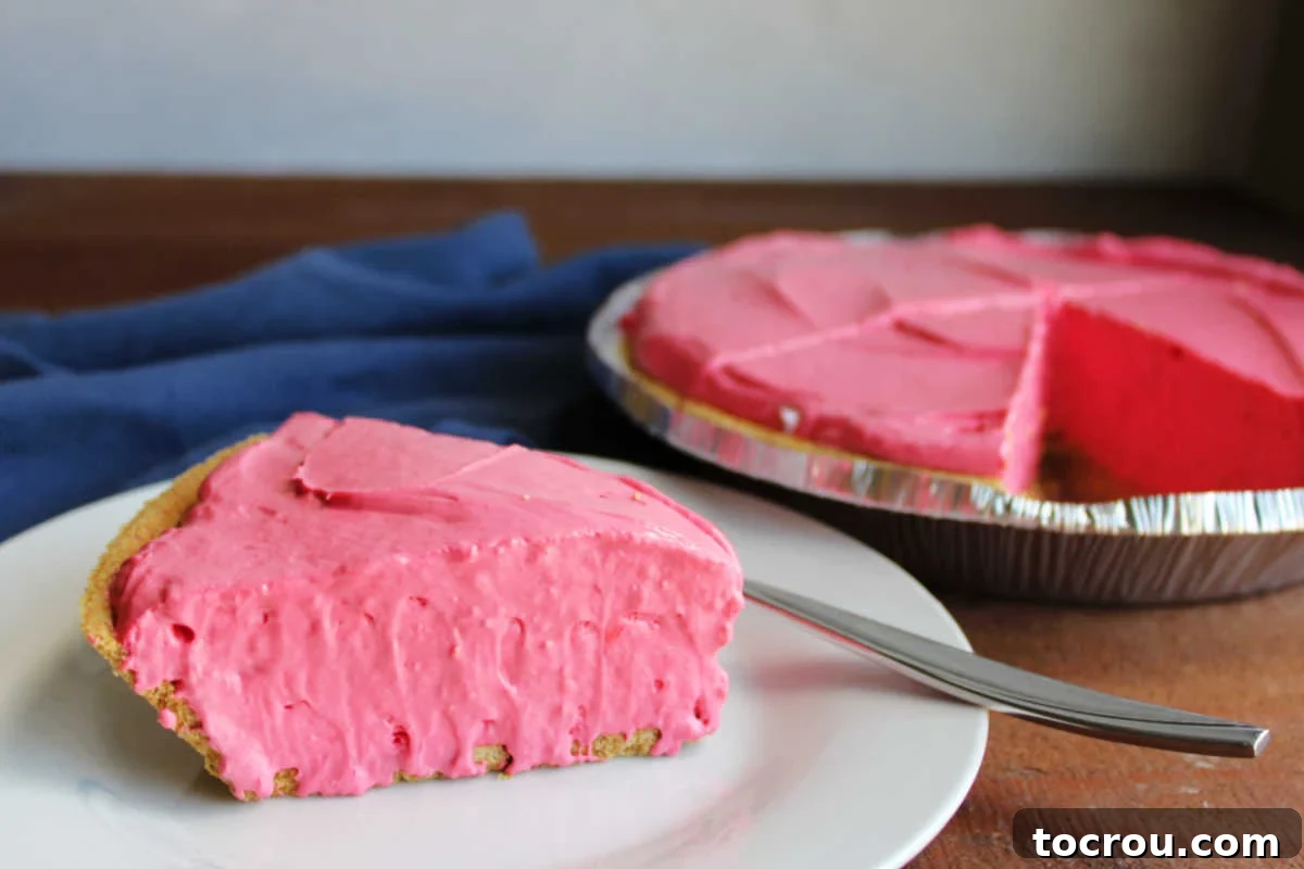 Bright pink fruit punch koolaid pie on plate with remaining pie in the background. 