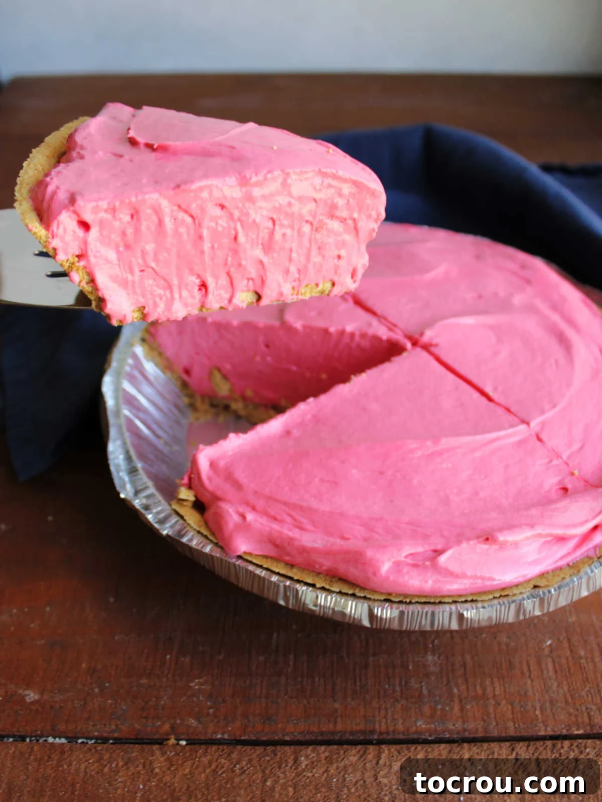 Pie server lifting piece of no-bake kool-aid pie out of the pie plate, ready to serve. 