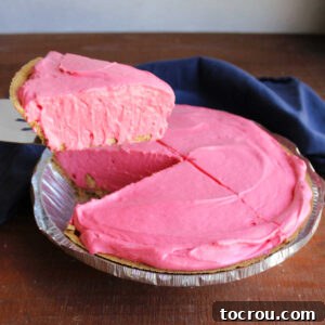 Lifting slice of creamy koolaid pie out of the dish showing bright pink fruit punch filling.