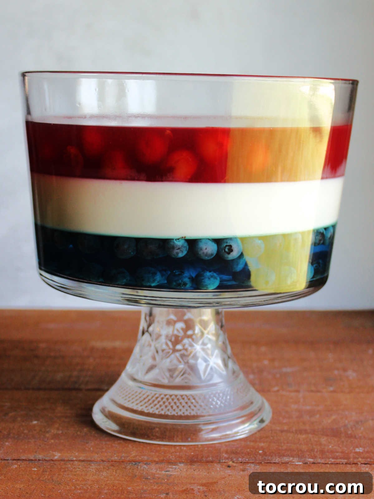 Patriotic Layered Jello 4 Close-up of the stunning layers of cherry Jello, blueberry Jello, and sweetened condensed milk Jello in a glass trifle dish, creating a festive red, white, and blue dessert masterpiece.