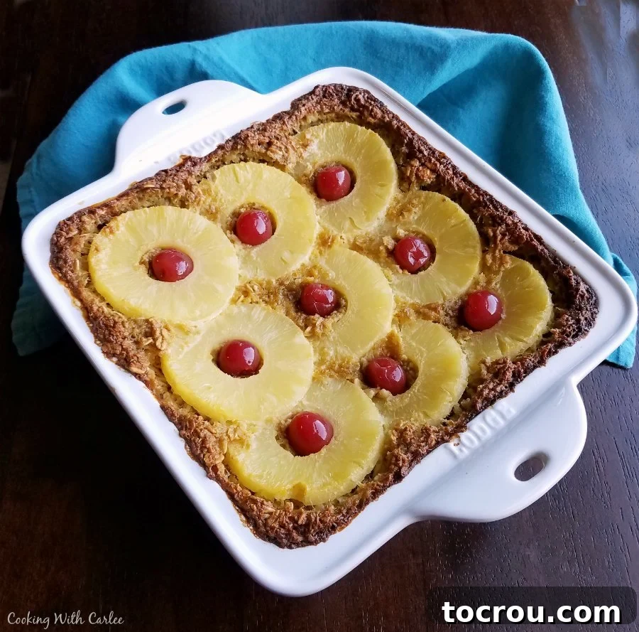 Sunny Pineapple Baked Oatmeal 3 A square baking pan brimming with freshly baked oatmeal, generously topped with glistening pineapple rings and bright red maraschino cherries, ready to be served. This fun breakfast offers a great creamy texture, hearty slices, and just enough sweetness to feel like a healthy treat.