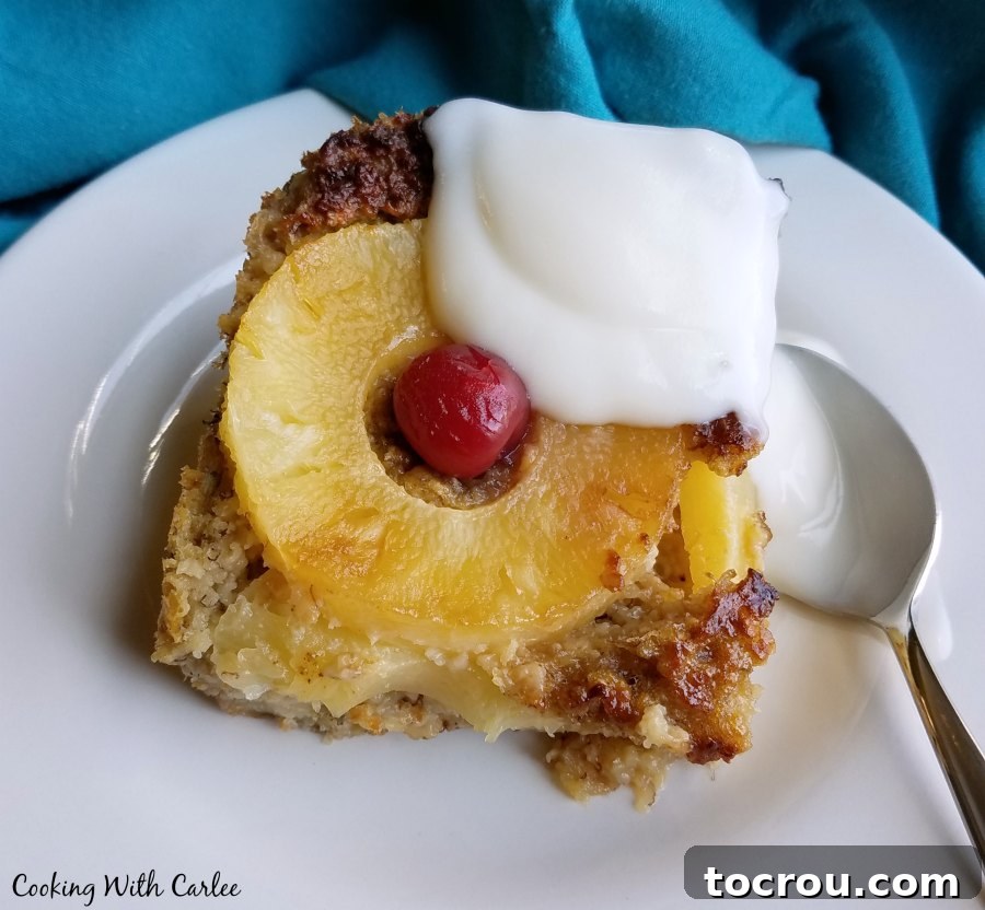 Sunny Pineapple Baked Oatmeal 4 A generous serving of pineapple baked oatmeal, artfully topped with a perfectly placed pineapple ring and a vibrant cherry, cleverly resembling a pineapple upside-down cake. This delicious and hearty breakfast is a comforting start to any day.