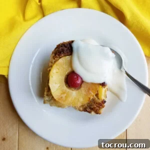 Piece of baked oatmeal topped with pineapple ring and marschino cherry served with some vanilla yogurt on a small plate.