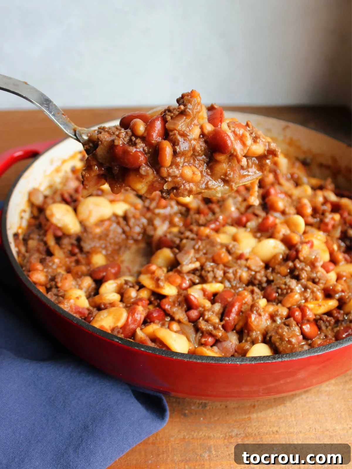Serving spoon lifting a heaping scoop of calico baked beans out of the pan. 