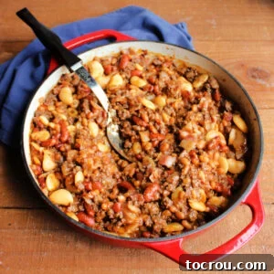Cast iron pan with calico beans featuring kidney beans, butter beans, and pork and beans with ground beef and bacon in a sweet and savory sauce.