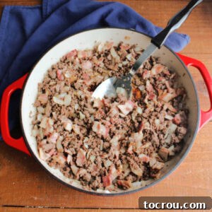 Cast iron skillet filled with browned ground beef, bacon, and diced onion.