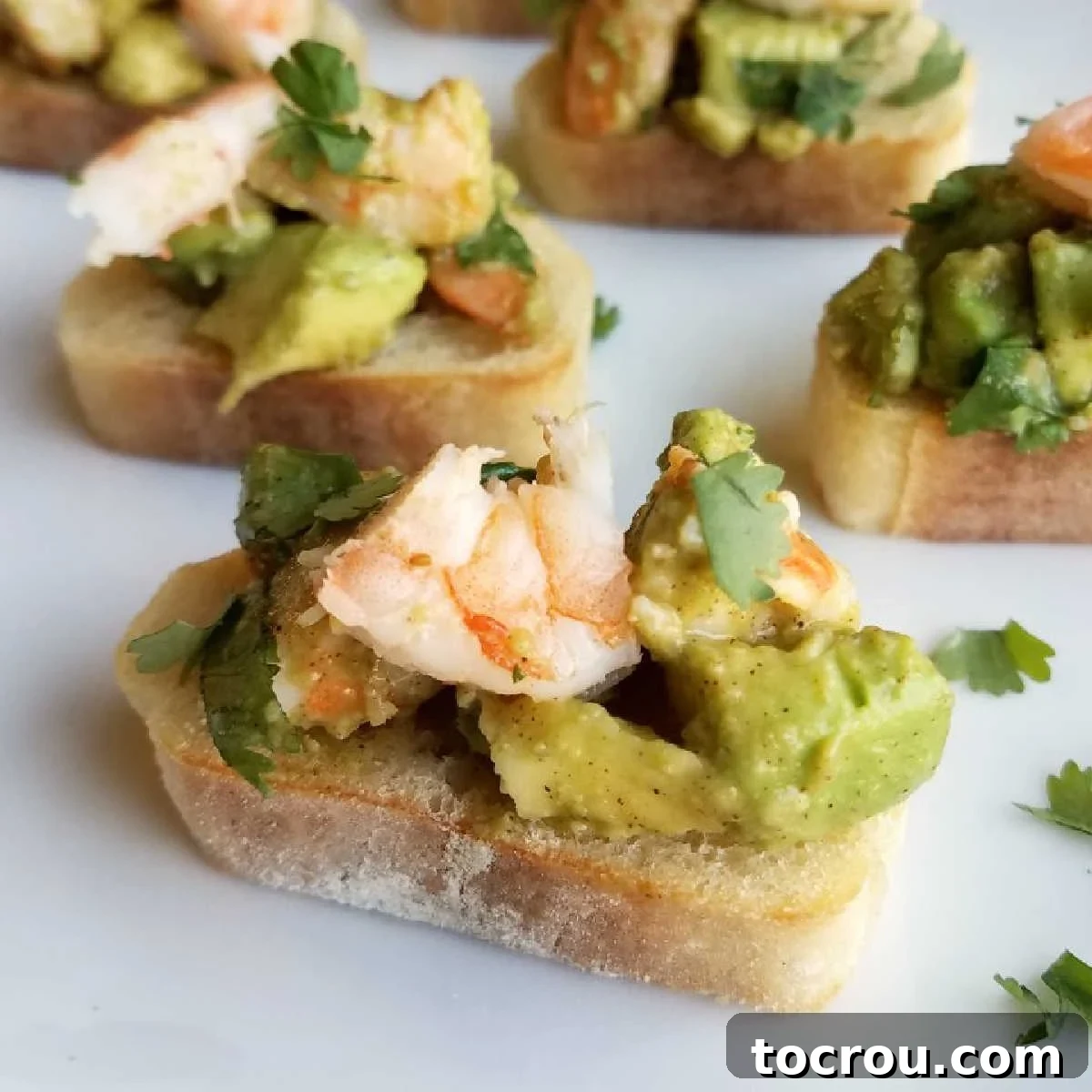 Avocado and Shrimp Crostini with fresh cilantro garnish Vibrant avocado and shrimp mixture delicately arranged on crispy baguette slices, garnished with fresh cilantro, ready to be served.