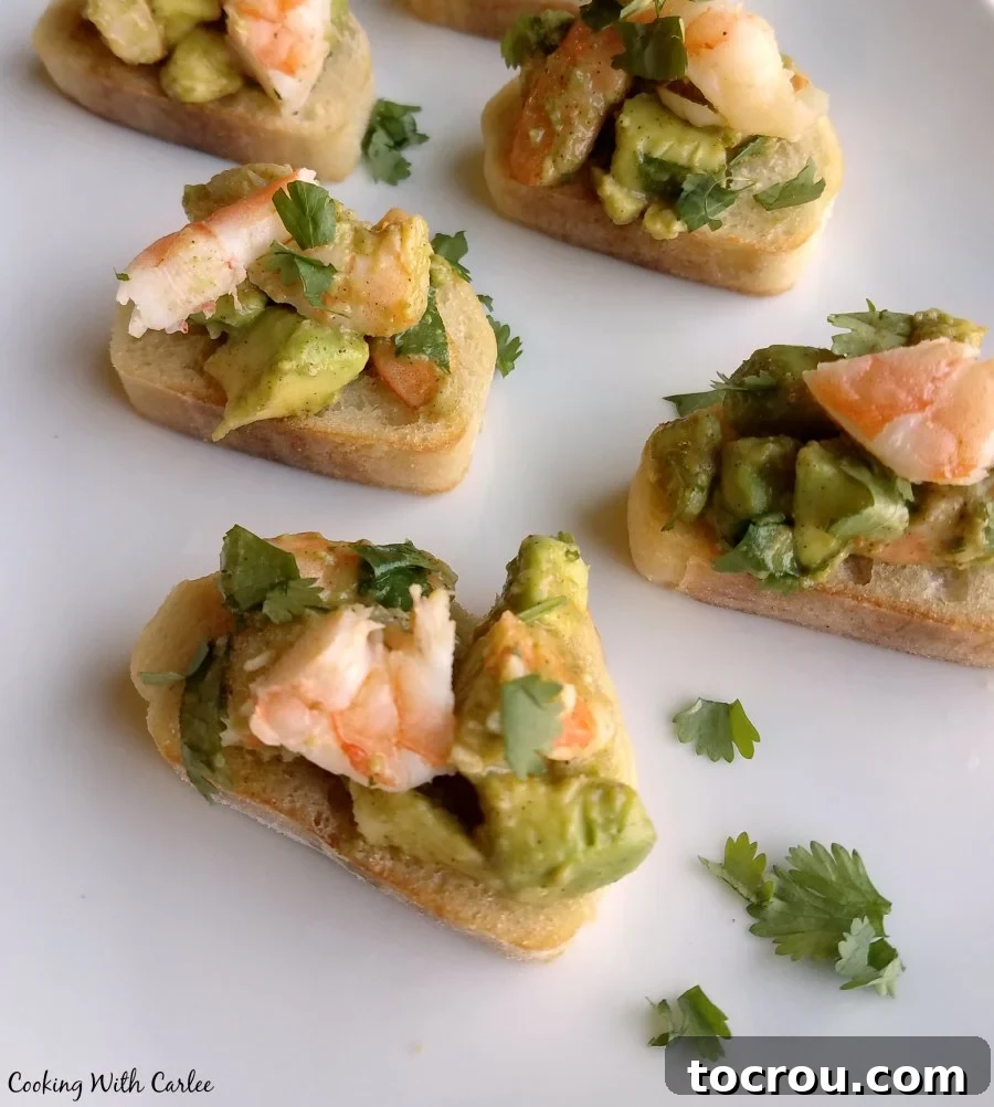 Delicious shrimp, creamy avocado, lime, cilantro and a hint of chili powder piled atop some delicious garlic bread. It is a one of a kind bruschetta appetizer that reminds me of our trip to the Houston shore. Close-up view of the avocado and shrimp mixture beautifully presented on toasted baguette slices, garnished with fresh cilantro, ready for serving.