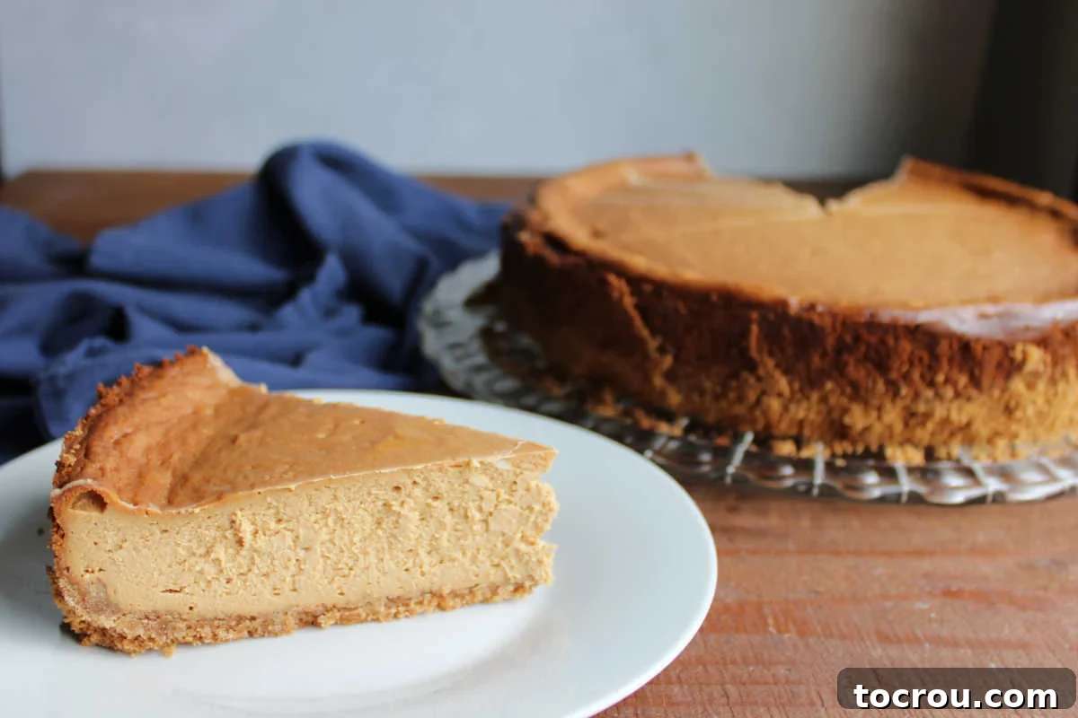 Slice of caramel colored dulce de leche cheesecake on plate by the rest of the cheesecake. 