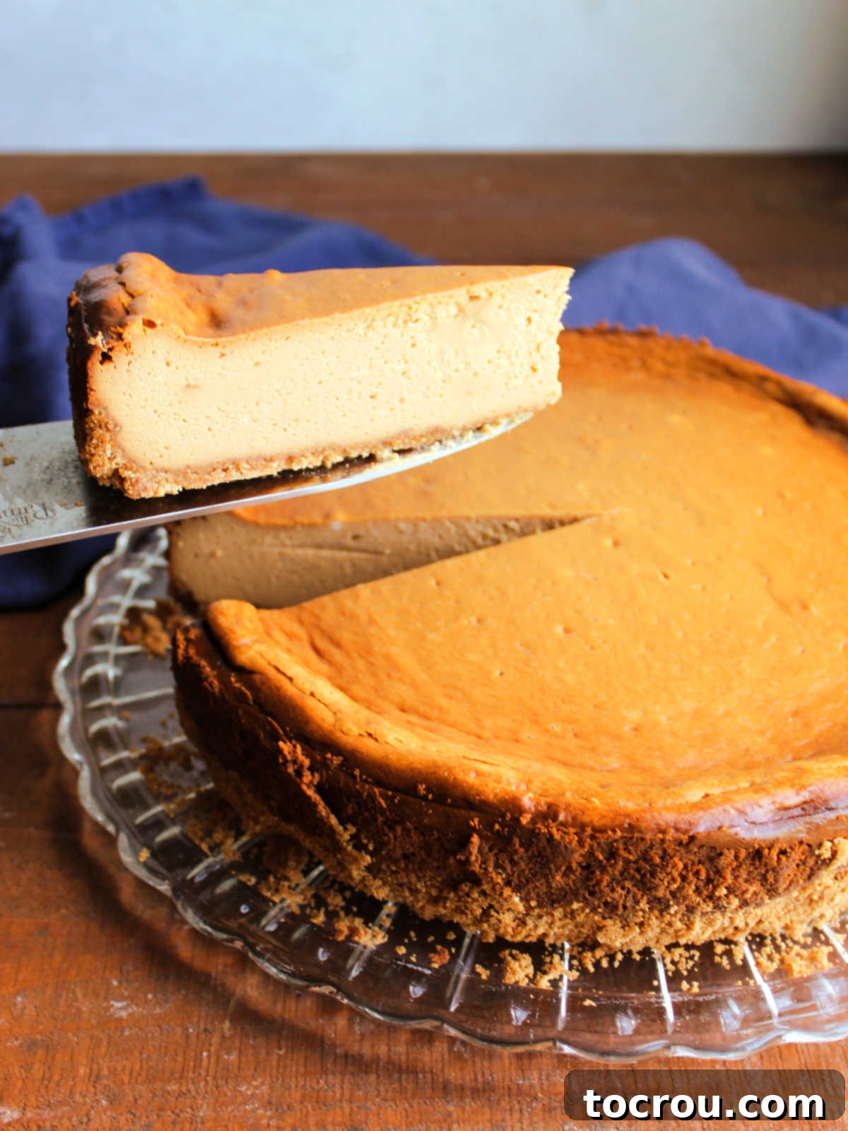 Lifting slice of dulce de leche cheesecake out of the whole cake showing smooth center and caramel color. 
