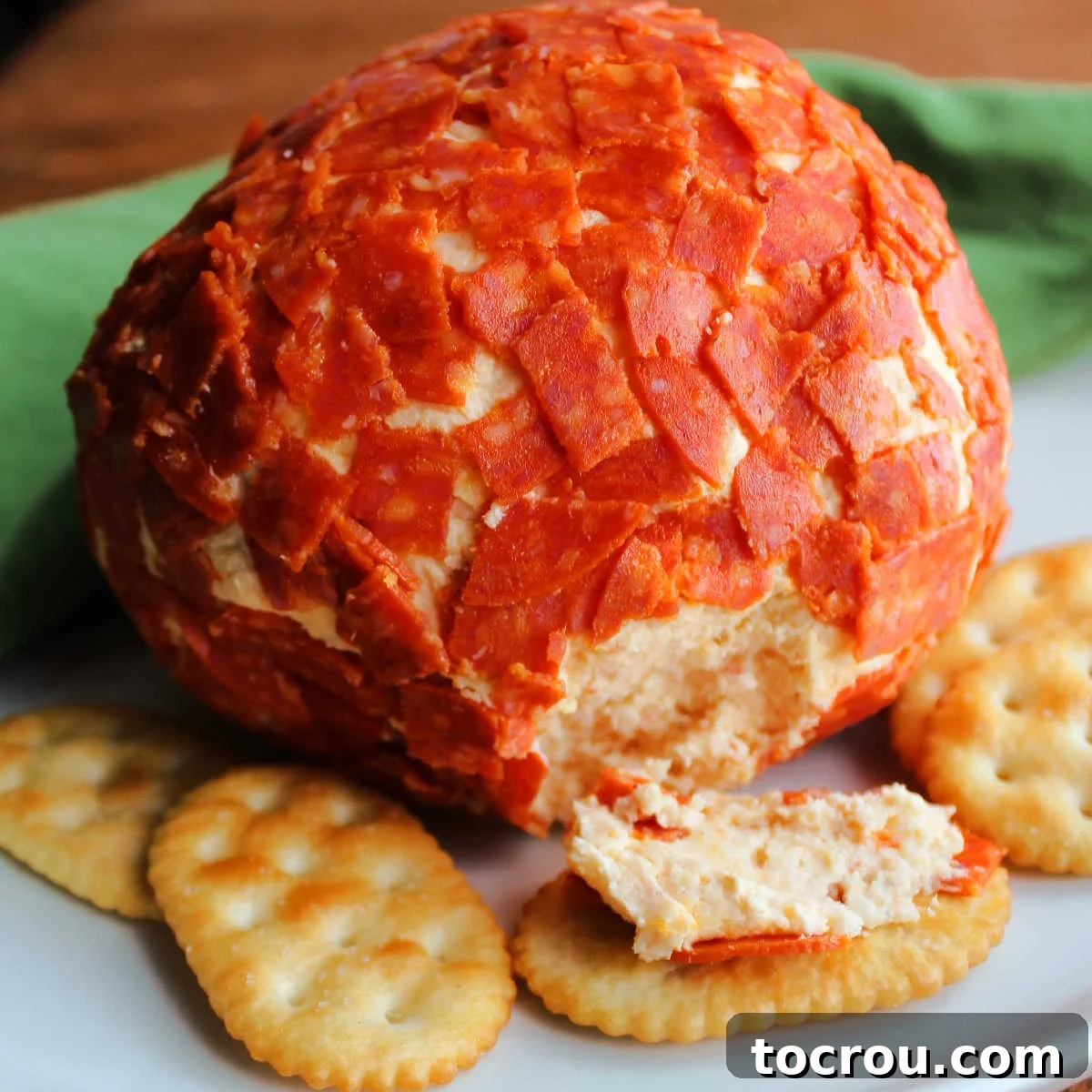 Cheeseball coated in chopped pepperoni next to crackers.