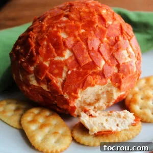 Cheeseball coated in chopped pepperoni next to crackers.