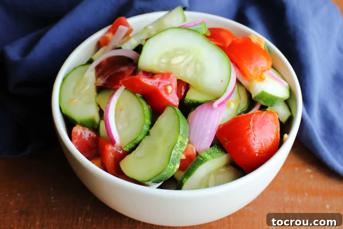 Bowl of cucumber, tomato, and onion salad in light homemade vinaigrette, ready to be served on a sunny day.