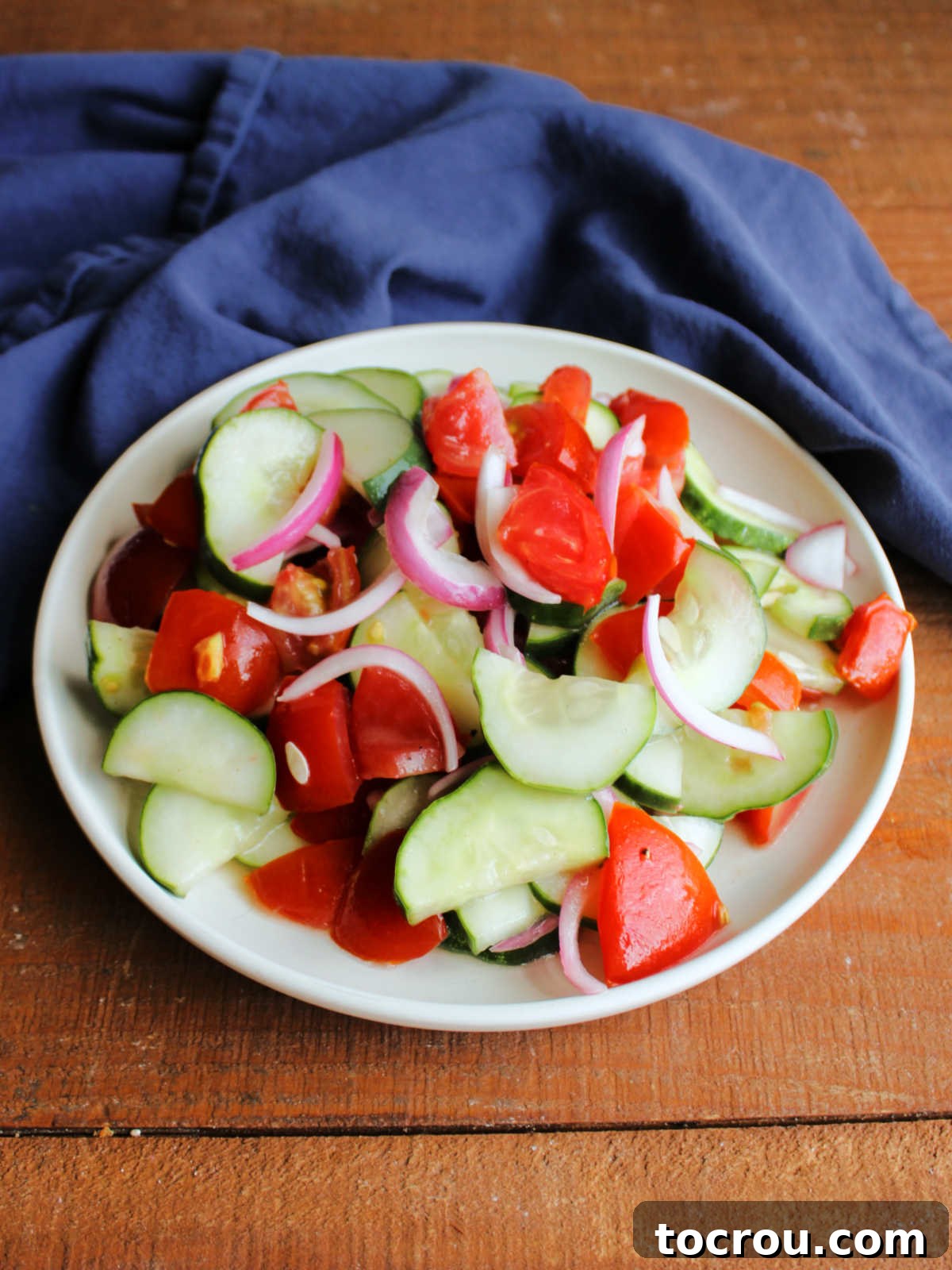 Plate with a serving of marinated tomato and cucumber salad, featuring red onion and a light vinaigrette dressing, presented ready to be eaten.