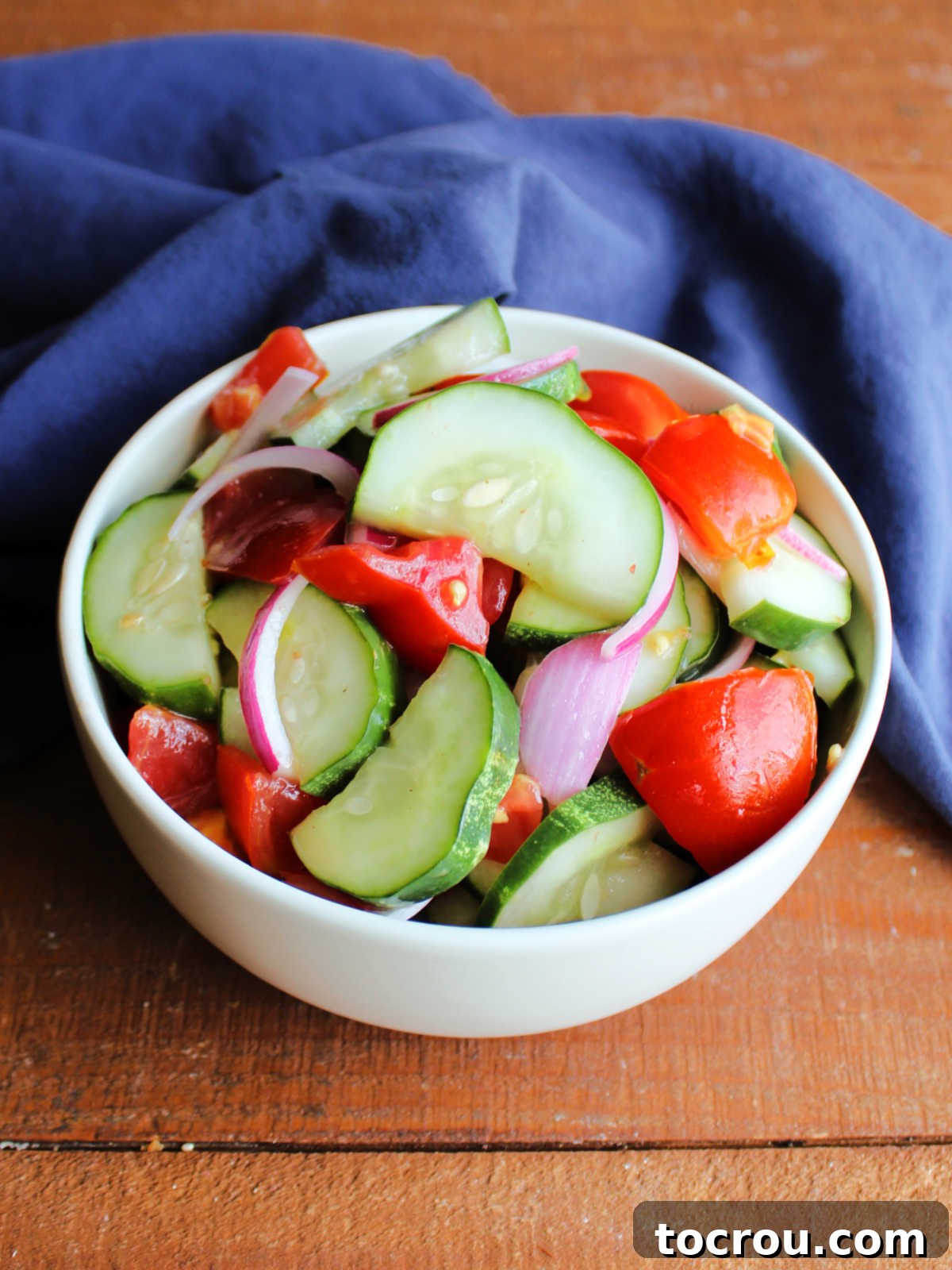 Large bowl filled with a generous amount of cucumber and tomato salad, enhanced with slivers of red onion and a glistening light dressing.